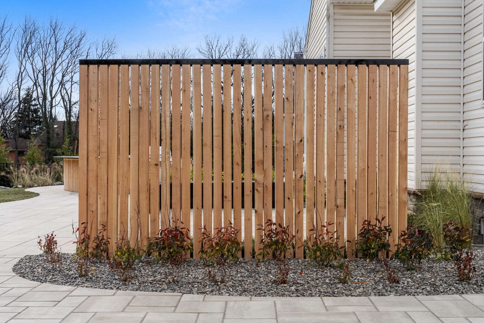 Cedar privacy screen behind a gravel planting bed beside a paver walkway