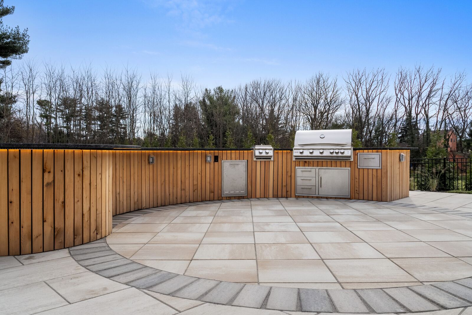 Circular paver inlay in front of a curved cedar outdoor kitchen with grill and refrigerator