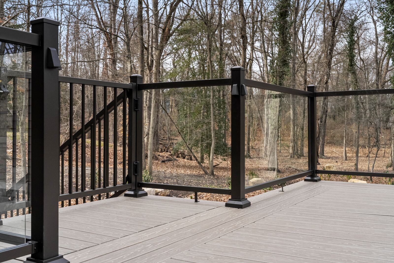 Corner of a composite deck with black-framed glass railings, overlooking the woods