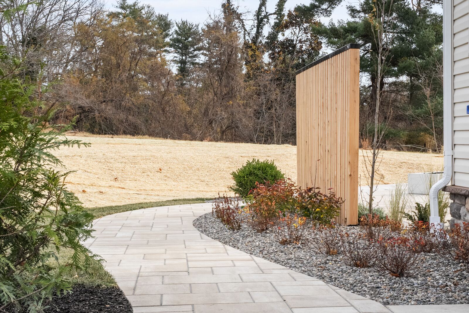 Curved paver walkway past gravel planting beds to a cedar privacy screen