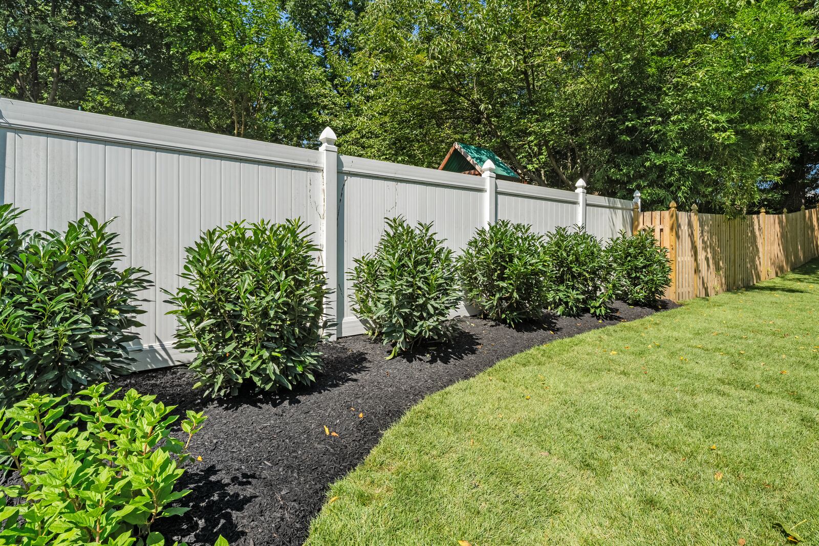 Curved, mulched shrub bed along a white vinyl fence beside a green lawn
