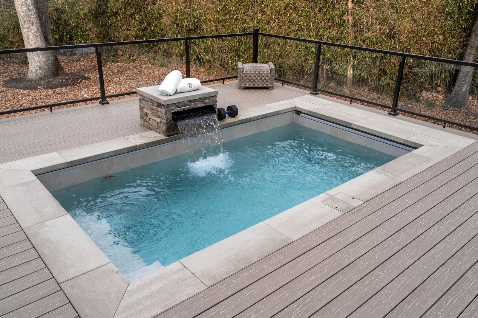 Compact plunge pool with a stacked-stone spillover, set into a composite deck with glass railings