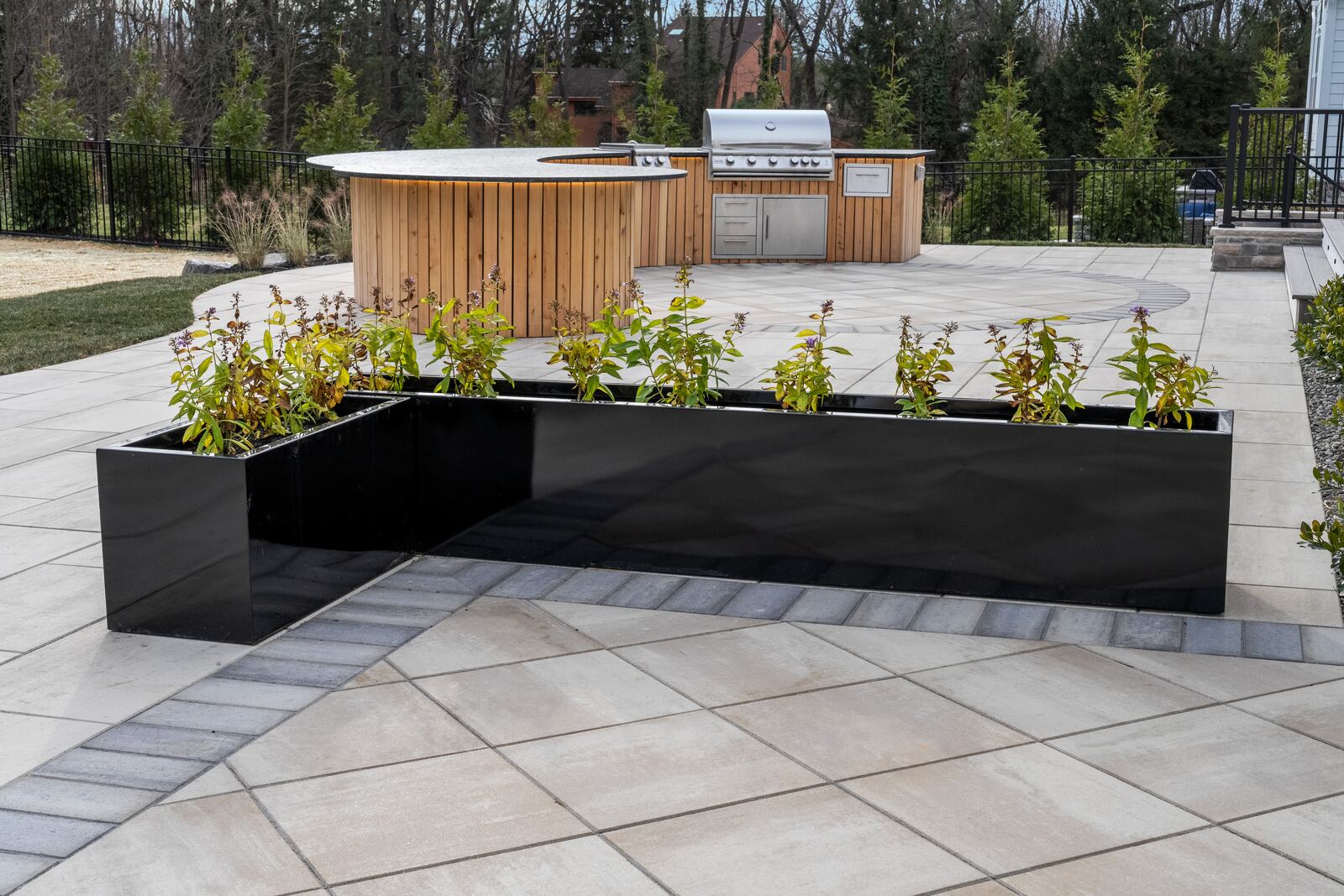 Black metal planters along a porcelain patio with a contrasting paver border