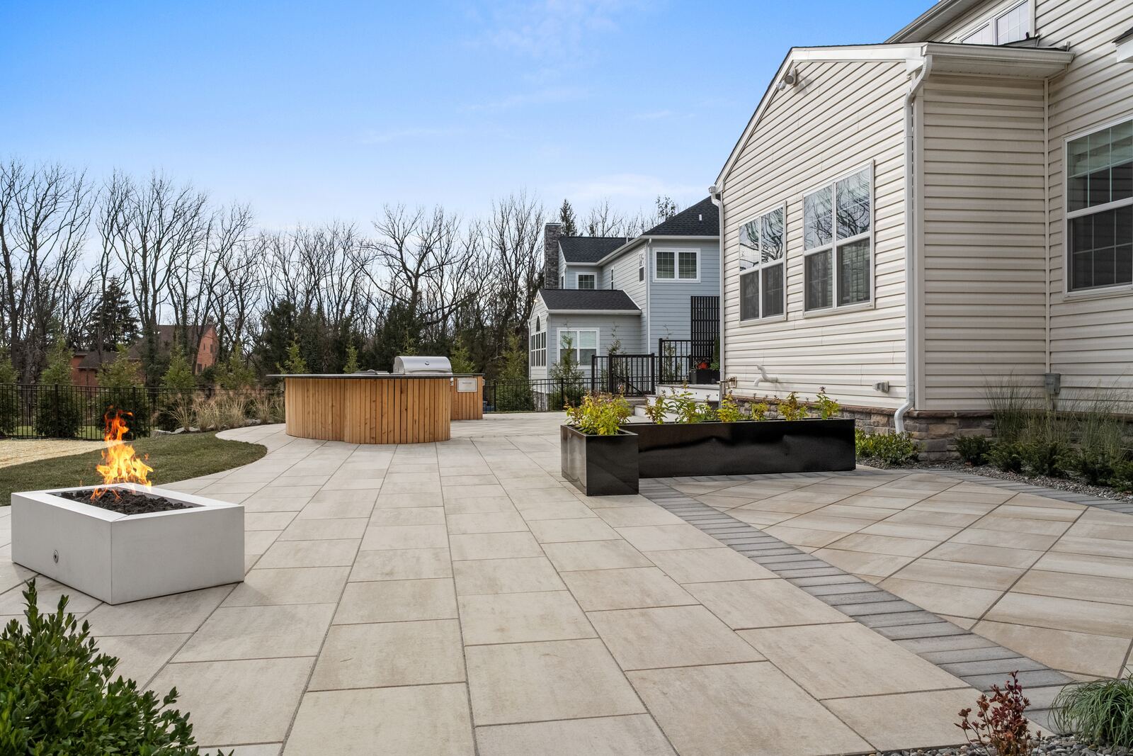 Large porcelain paver patio with a concrete fire table, black planters and a curved outdoor kitchen