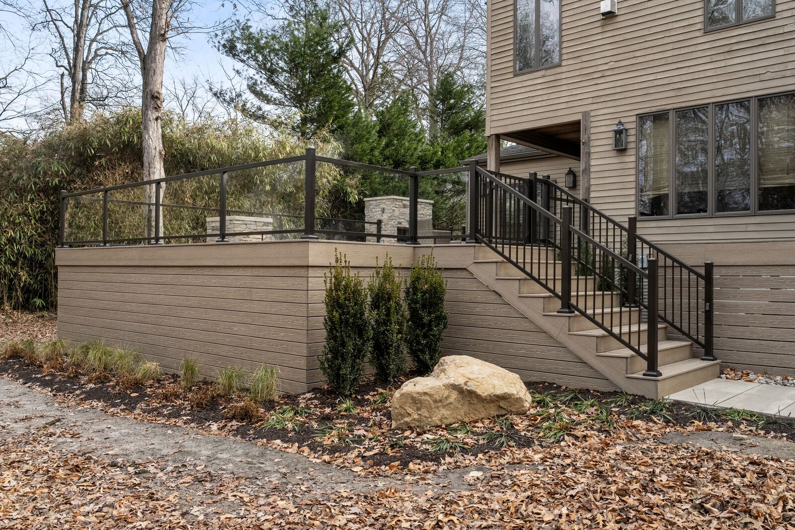 Raised composite deck over a new bed of arborvitae, boulders and mulch