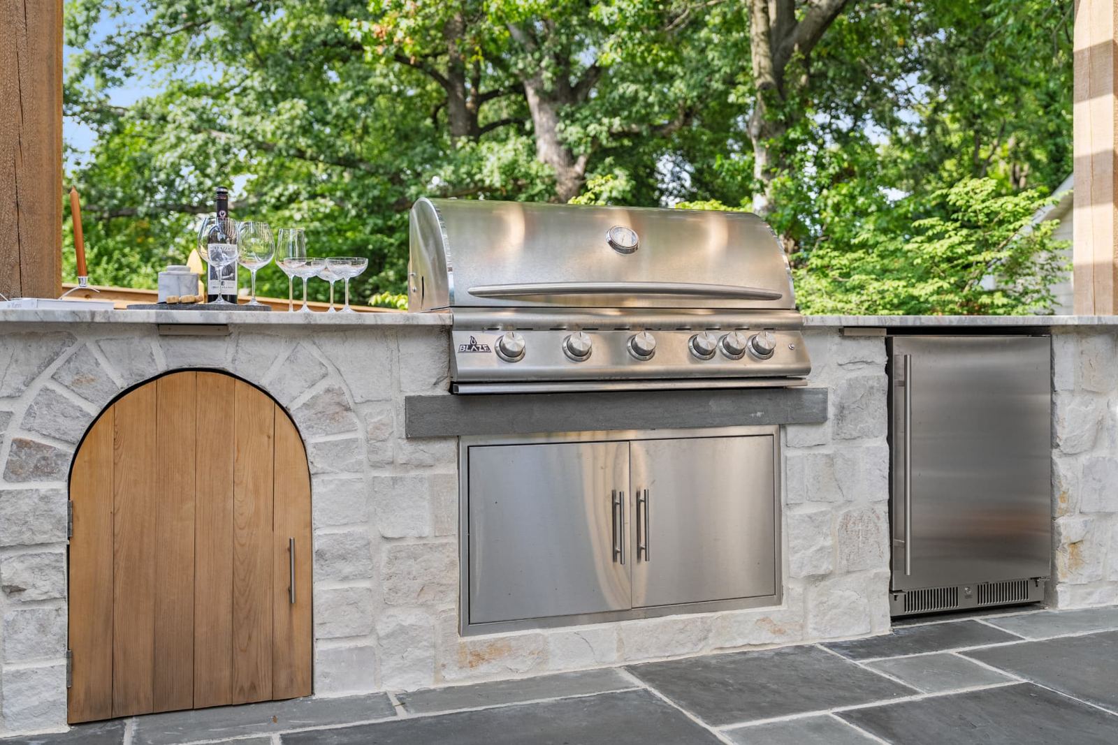 Stone outdoor kitchen with built-in grill, refrigerator and bluestone patio