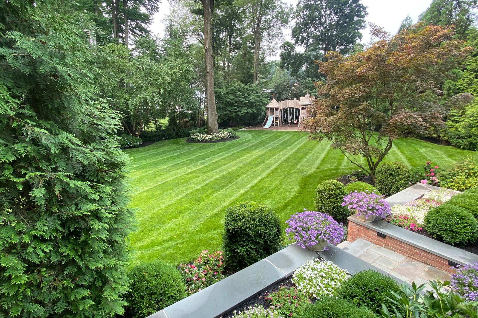 Freshly mowed backyard lawn with crisp stripes, bordered by boxwoods, planting beds and mature trees